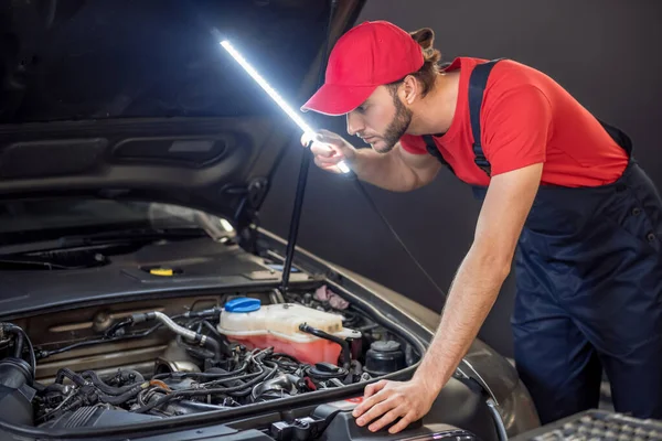Man with special lamp under hood of car — Stock Photo, Image