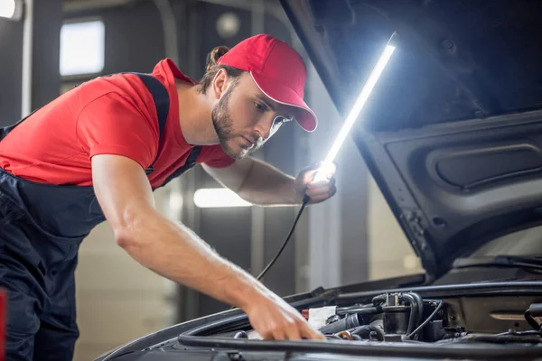 Auto mechanic with lamp checking car anatomy — Stock Photo, Image