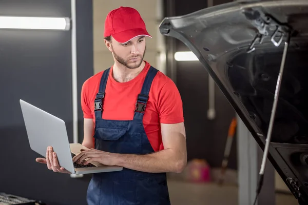 Auto monteur met laptop op zoek onder de motorkap — Stockfoto