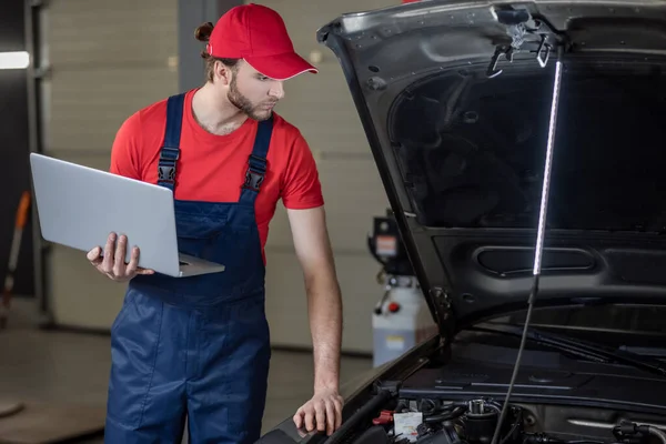 Hombre con ordenador portátil comprobar la anatomía del coche — Foto de Stock