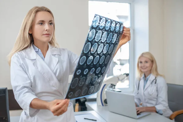 Läkare undersöker MRT scan och kollega på bärbar dator — Stockfoto