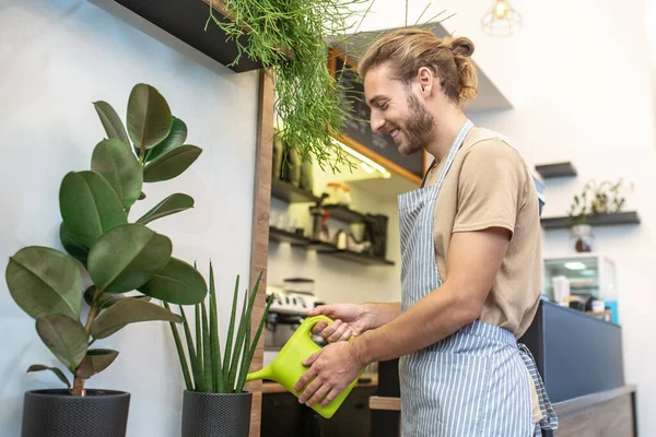 Lächelnder Mann im Profil gießt Pflanzen im Café — Stockfoto