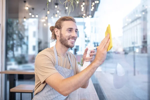 Lächelnder Mann wischt nachmittags Fenster in Café ein — Stockfoto