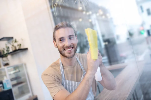 Feliz joven limpiando vidrio mientras está en la cafetería —  Fotos de Stock