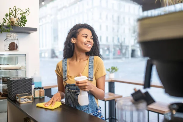 Mujer limpiando la superficie en la cafetería mirando a un lado —  Fotos de Stock