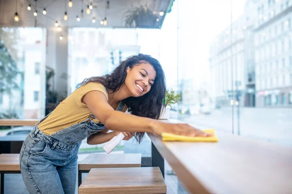 Mujer joven limpiando diligentemente la superficie de la mesa — Foto de Stock