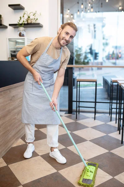 Junger Mann putzt mit Wischmopp das Café — Stockfoto