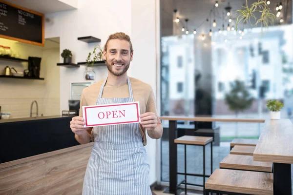 Homem sorridente segurando sinal que diz aberto — Fotografia de Stock