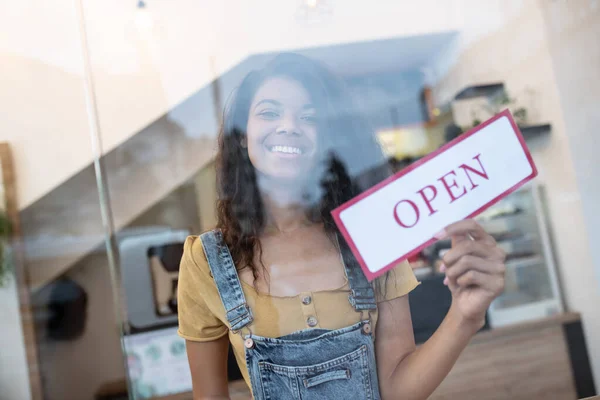 Kvinna bakom glas inne café med skylt i handen — Stockfoto