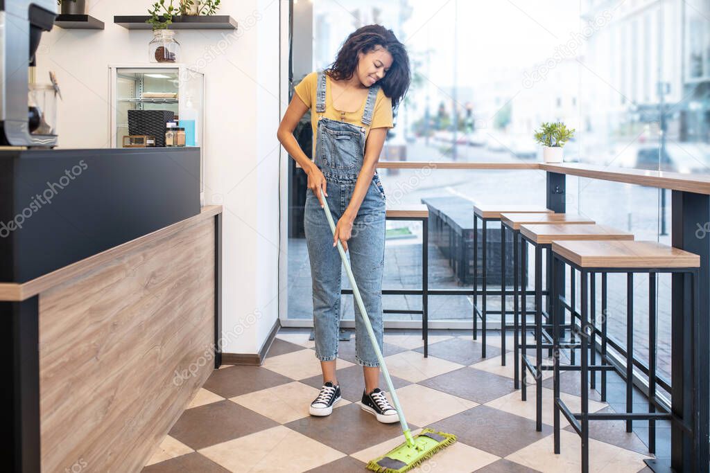Young woman mopping floor in cafe