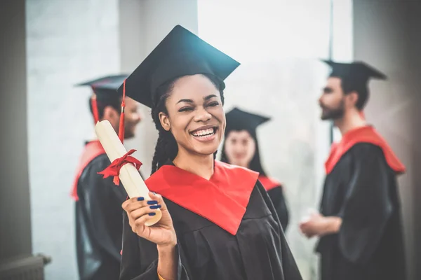 Cute african american girl in mortarboard looking happy and smiling nicely — Stock Photo, Image