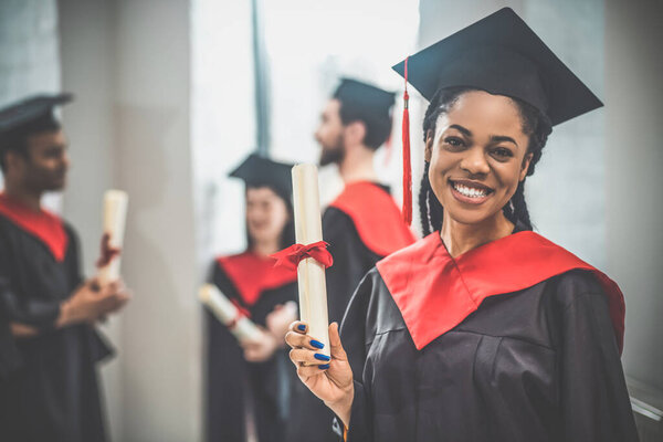 Симпатичная африканская американка в миномётной доске выглядит счастливой и красиво улыбающейся.