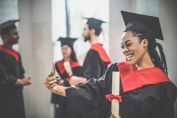 Cute african american girl in mortarboard looking happy and smiling nicely — Stock Photo, Image