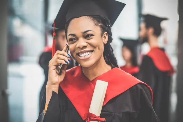 Glimlachende afgestudeerde met een donkere huid aan de telefoon — Stockfoto