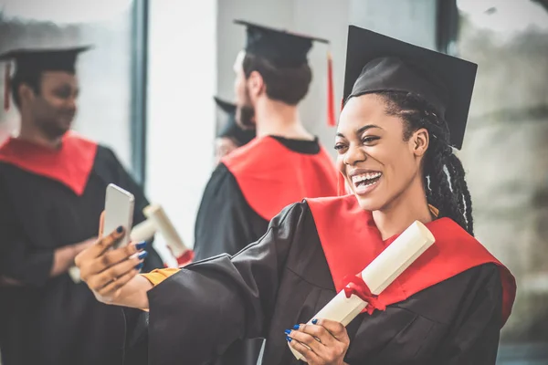 Smiling girl in mortarboard making selfie and looking happy — Stock Photo, Image