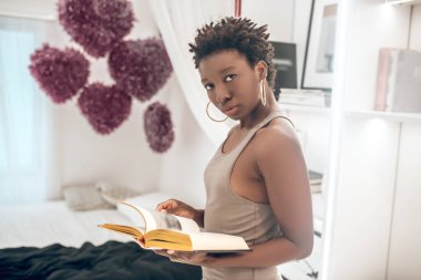 Zarif, güzel, esmer tenli, elinde kitap olan bir kadın.