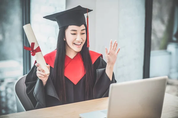 졸업장을 들고 있고 비디오 전화를 받고 있는 귀여운 아시아인의 미소 — 스톡 사진