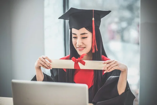 졸업장을 들고 있고 비디오 전화를 받고 있는 귀여운 아시아인의 미소 — 스톡 사진