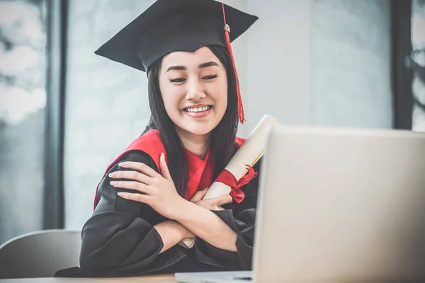 Cute asian smiling graduate holding her diploma and looking happy