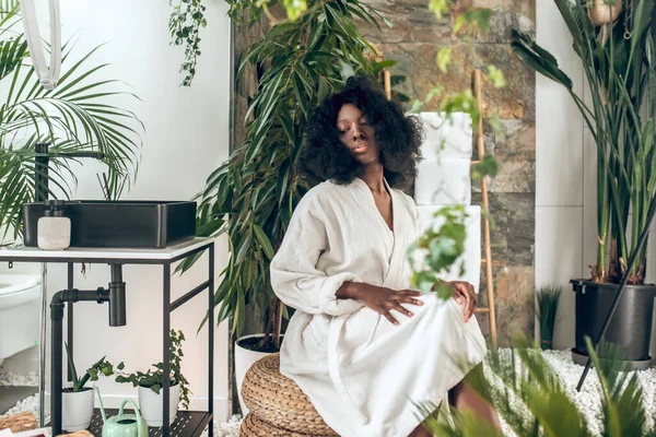 Beautiful dark-skinned woman in na bath robe looking enjoyed and pleased