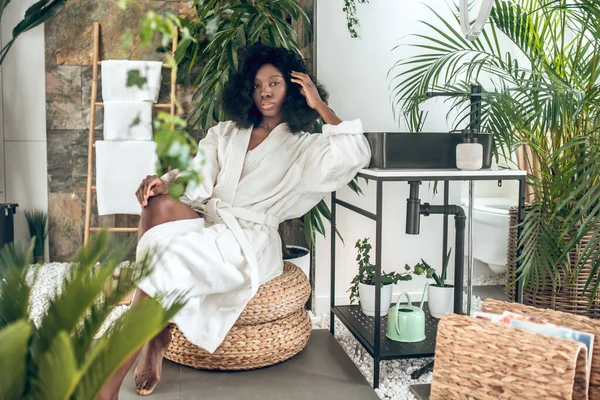 Banyo bornozu giymiş güzel, esmer bir kadın. Keyif alıyor ve memnun görünüyor.