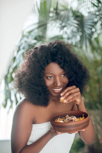 Beautiful young woman covered in a white towel holding a bowl with flowers petals — Stock Photo, Image