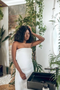 Koyu tenli güzel bir kadın saçını tarıyor ve kendini rahat hissediyor.