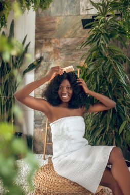 Koyu tenli güzel bir kadın saçını tarıyor ve kendini rahat hissediyor.