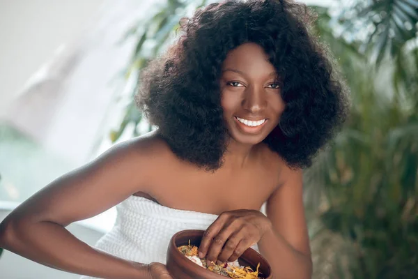 Beautiful young woman covered in a white towel holding a bowl with flowers petals — Stock Photo, Image