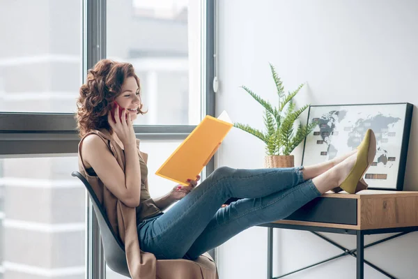 Giovane donna che lavora a un progetto e ne discute con un collega al telefono — Foto Stock