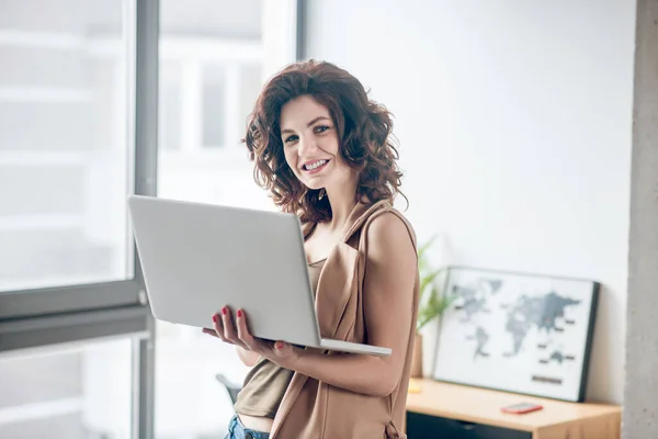 Mujer guapa de cabello oscuro trabajando en un portátil y luciendo contenta — Foto de Stock