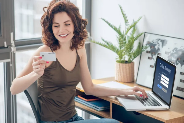 Mujer bonita sosteniendo una tarjeta de crédito y planeando hacer pagos en línea — Foto de Stock