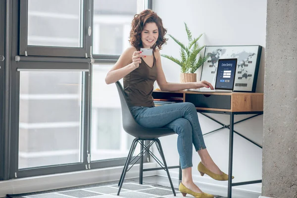 Mujer bonita sosteniendo una tarjeta de crédito y planeando hacer pagos en línea — Foto de Stock