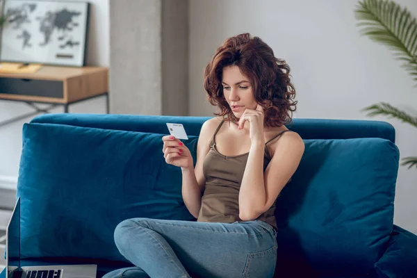 Mujer joven sosteniendo una tarjeta de crédito y planeando comprar algo en línea — Foto de Stock