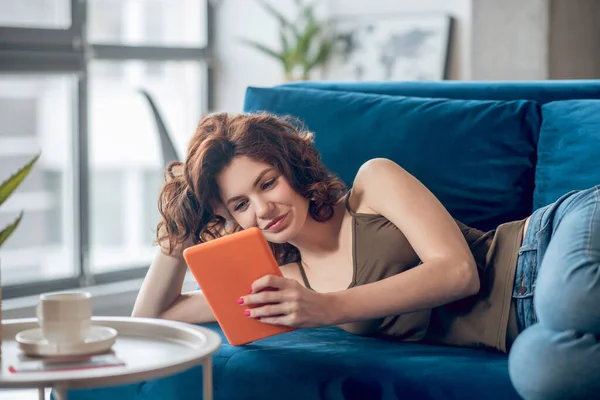 Vrouw liggend op een bank met een tablet in handen — Stockfoto