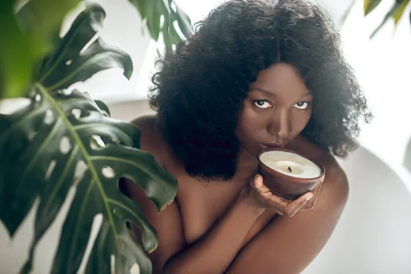 Naked dark-skinned woman smelling an organic candle — Stock Photo, Image