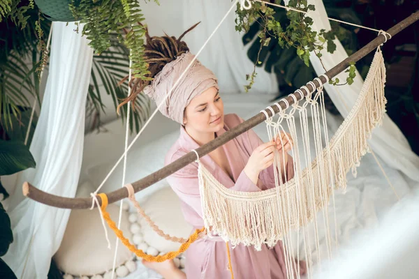 Mujer joven en una ropa de cabeza buscando concentrado mientras teje macramé —  Fotos de Stock