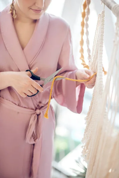 Woman in a headwear cutting yarn while weaving macrame — Stock Photo, Image