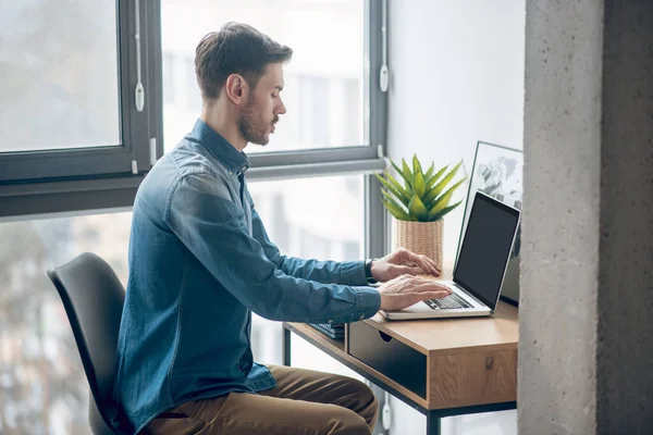 Hombre moreno sentado en la mesa y trabajando en un portátil — Foto de Stock