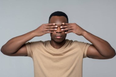 Ayakta duran adam elleriyle gözlerini kapatıyor.