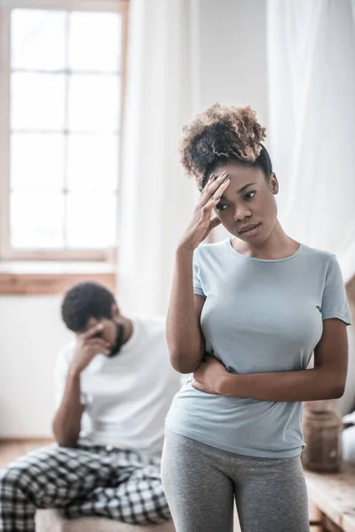 Afro-americana mujer pensativa de pie y marido sentado detrás — Foto de Stock