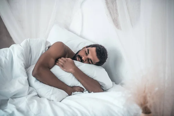 Hombre de piel oscura durmiendo abrazando almohada en el dormitorio — Foto de Stock