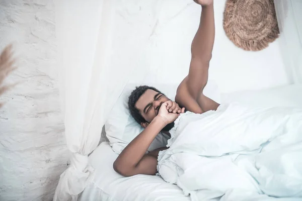 Mörkt gäspande man liggande i vit säng — Stockfoto