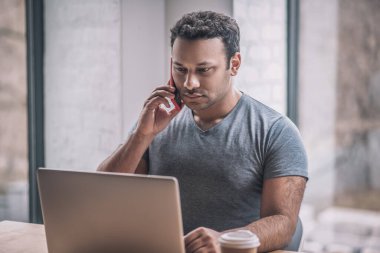 Genç işadamı ofiste masada oturuyor ve telefonda konuşuyor.