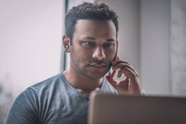 Genç işadamı ofiste masada oturuyor ve telefonda konuşuyor.