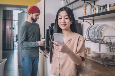 Şirin Asyalı kız iş arkadaşlarıyla kahve içiyor ve mesajlaşıyor.