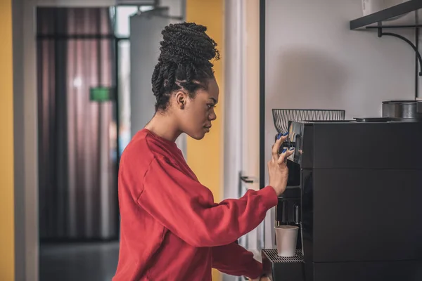 Mörkhyad ung kvinna står nära kaffemaskinen — Stockfoto