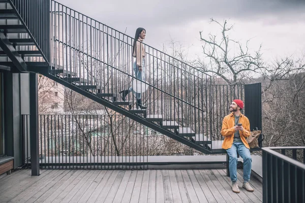 Мужчина сидит на ступеньках, девушка спускается по мосту — стоковое фото