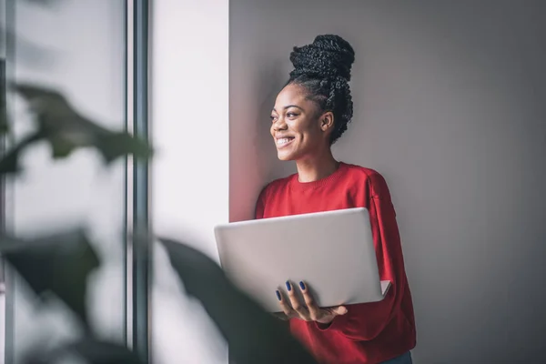 Femme noire en chemise rouge avec un ordinateur portable travaillant à distance — Photo