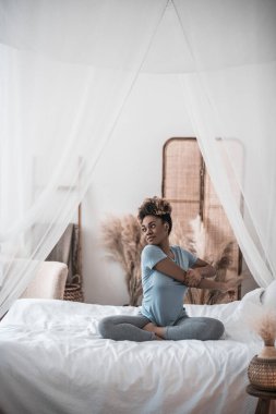 Kadın sabah antrenmanı yapıyor, yatakta oturuyor.